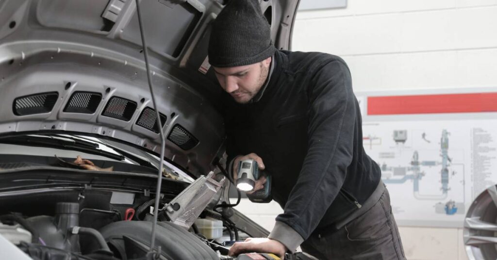 A man wearing black jacket performing a regular car maintenance check on a vehicle.