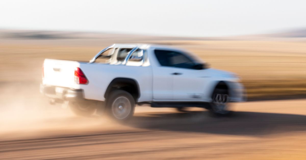 White HiLux driving quickly down a dirt road.