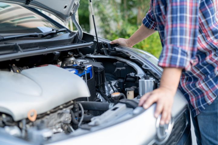 A person is inspecting a car engine with the hood open, possibly performing maintenance or checking for issues.