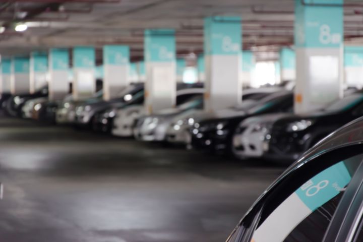 A row of parked cars in an underground parking garage with teal and white column signs indicating the section number.