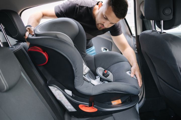 A man installs a child car seat in the back seat of a vehicle, carefully securing it in place.